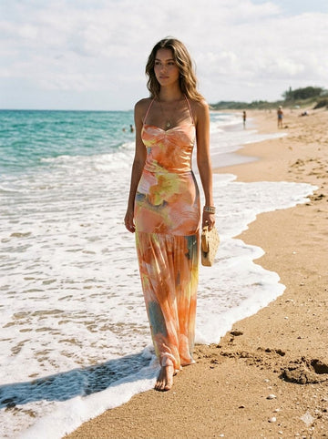 Summer Dress Trends 2026: Woman in vibrant watercolor print maxi dress with woven bag walking on beach, showcasing aesthetic style to shine under the sun.