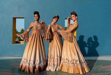 Three women in golden gowns stand against blue wall