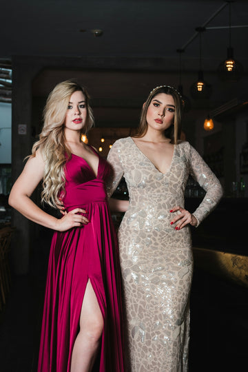 Two women in formal evening gowns posing in a dimly lit restaurant