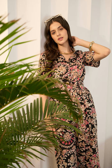 Woman in floral jumpsuit leans against wall