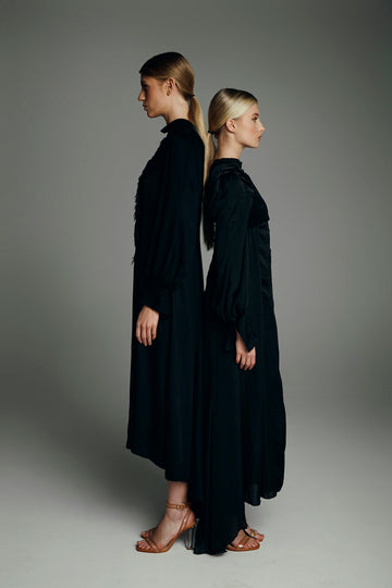 Two women in black dresses stand back-to-back
