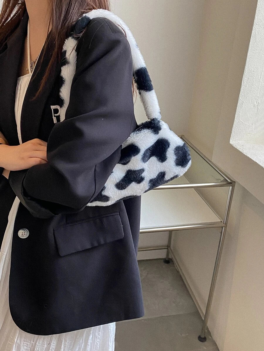 Cow-print plush baguette handbag with padded handle resting on cream chair