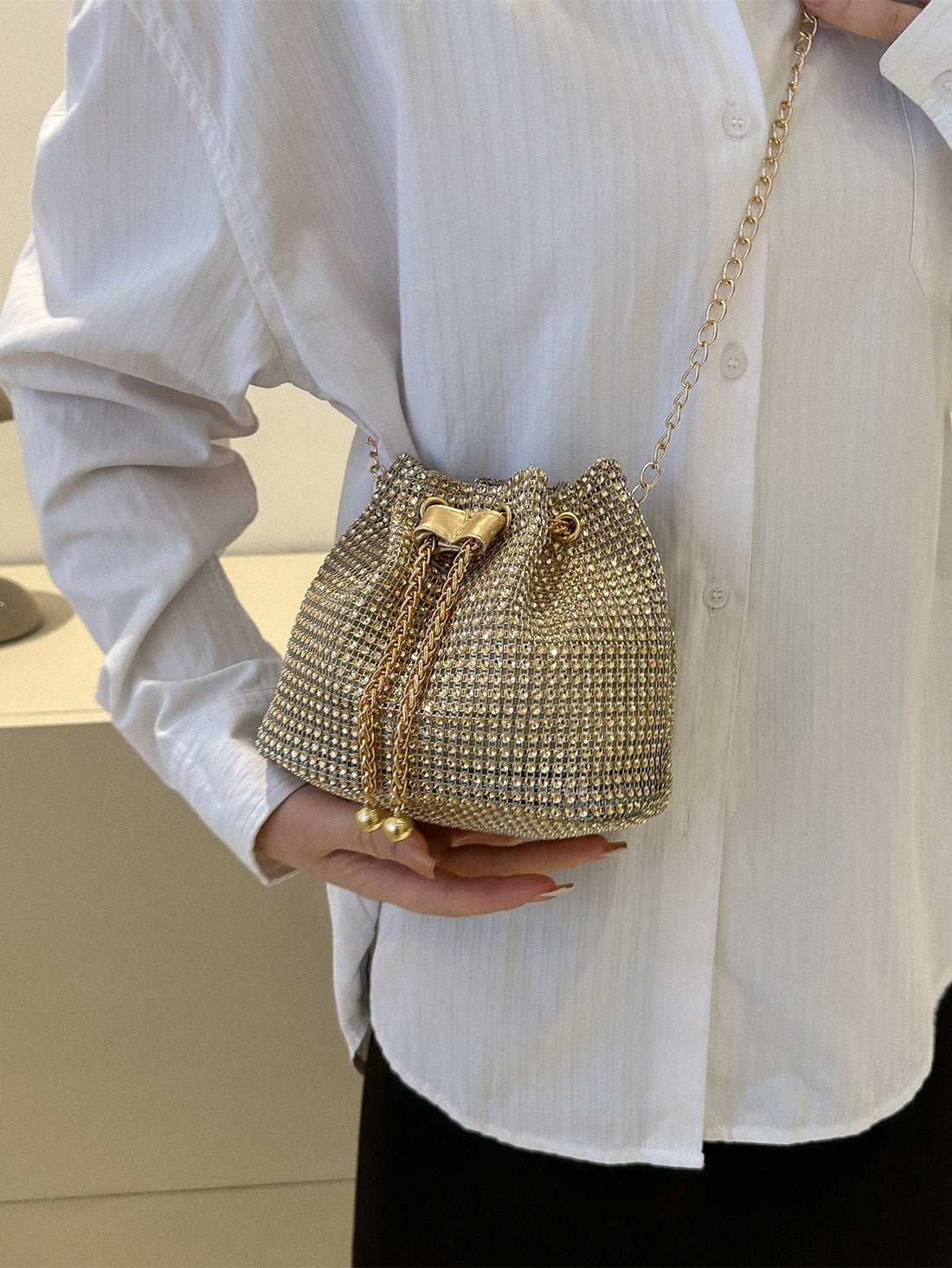 Get ready to dazzle with the Sparkling Elegance mini bucket bag. This glamorous bag features a drawstring closure and is adorned with shimmering rhinestones, making it the perfect accessory for any bridal or evening look. Elevate your style with this stunning and elegant piece.