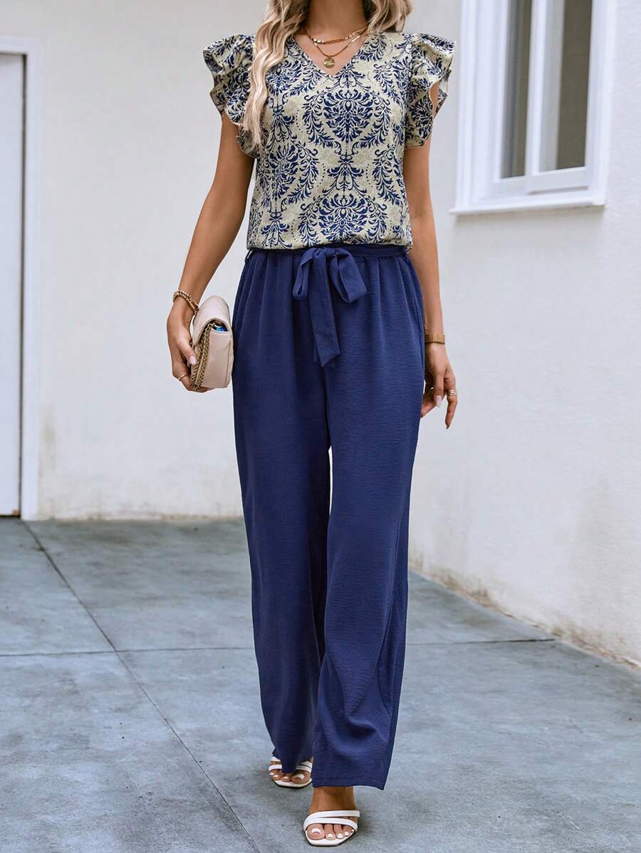 Elevate your vacation wardrobe with this chic 2-piece set featuring a navy blue blouse and coordinating pants. The flounce-sleeved blouse showcases a flattering V-neckline, tiered layers, and ruffle details for effortless elegance. The high-waisted pants come with a matching belt to cinch your silhouette. Crafted from a comfortable polyester-elastane blend, this set transitions seamlessly from casual outings to office settings. 