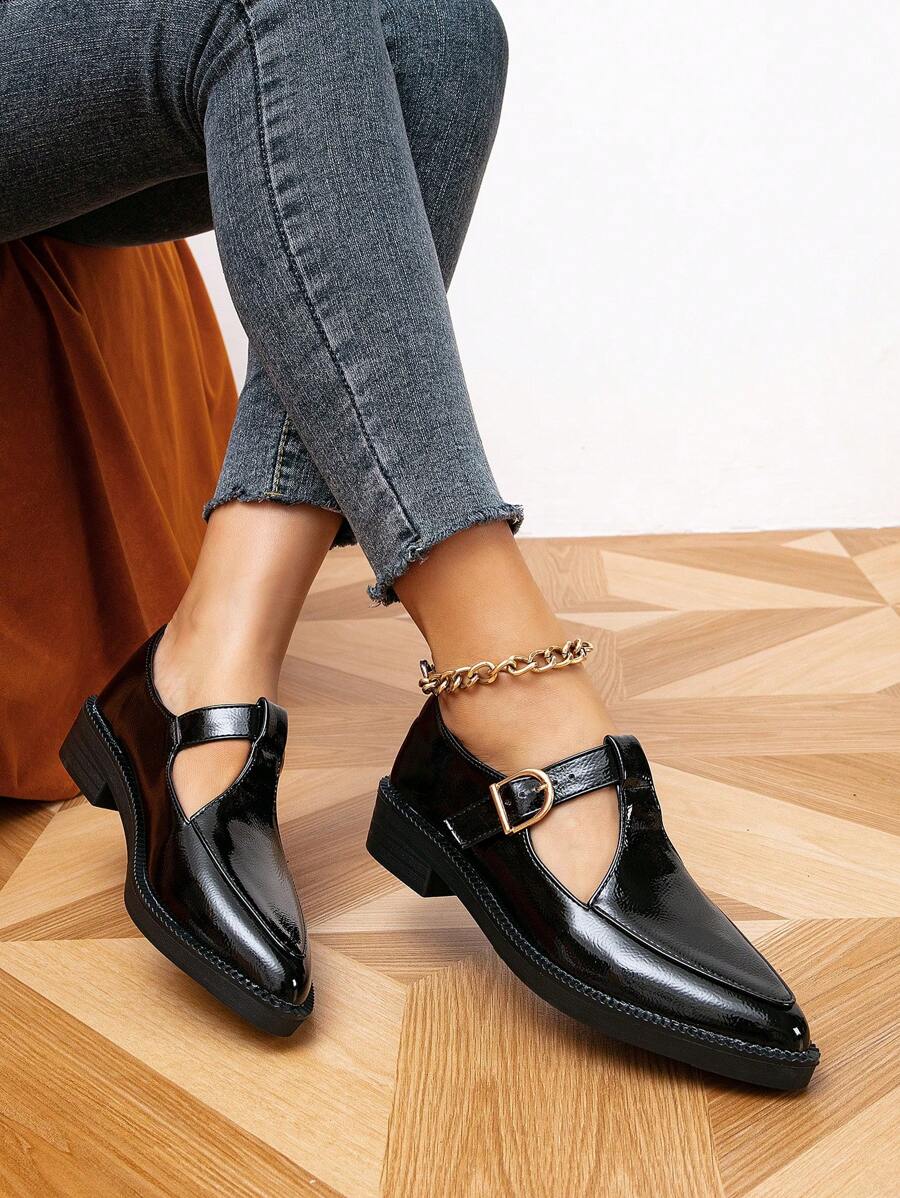 Front view of solid black T-strap flats with pointed toes and gold buckles