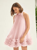 A woman wearing a light pink sleeveless tulle dress with a high gathered neckline, bow detail, and a ruffled flower-trimmed hem, photographed against a clean off-white background.