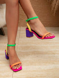 Model wearing bright multicolor ankle-strap block heel sandals with pink soles orange toe straps green ankle straps and purple heels