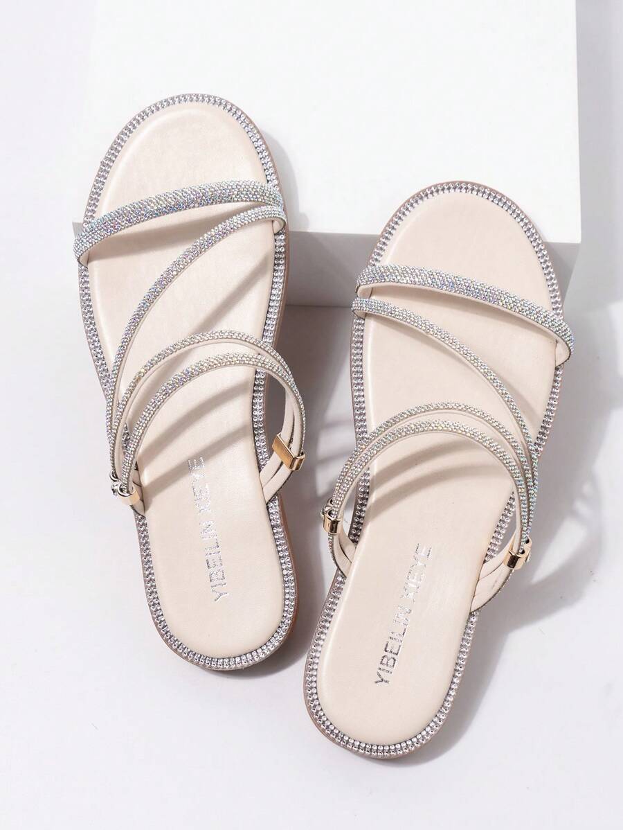 Top view of beige flat sandals with crisscross rhinestone straps and gold loop hardware