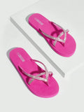 Overhead product view of hot pink rhinestone flip flops on a white plinth