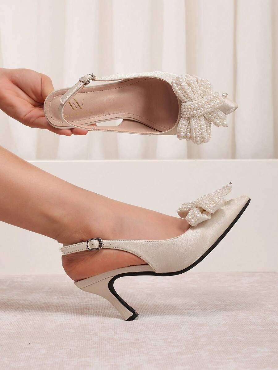 Hand-held view of cream pearl bow kitten heel pump