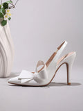 5 media show white patent pointed toe slingback pumps with high stiletto heel, open back, slim slingback strap with elastic insert, large structured bow on vamp, glossy faux patent leather, nude insole, tan outsole and brown heel tip. image 5