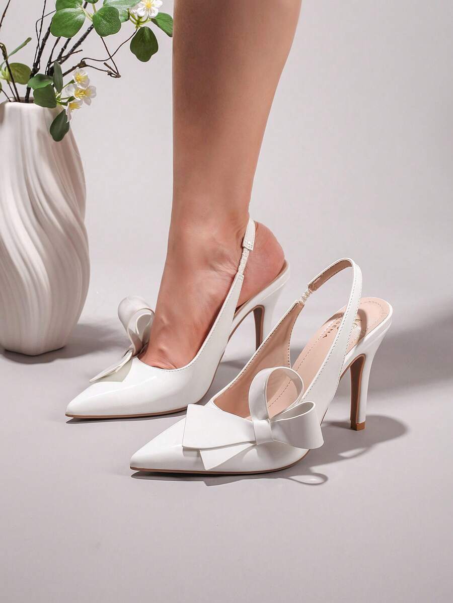 5 media show white patent pointed toe slingback pumps with high stiletto heel, open back, slim slingback strap with elastic insert, large structured bow on vamp, glossy faux patent leather, nude insole, tan outsole and brown heel tip. image 4