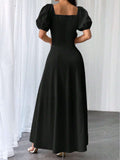 A woman wearing a long black dress with puff sleeves and a square neckline, shown from the back in a studio setting with white curtains and a gray floor.