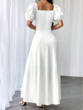 A woman wearing a white maxi dress with puff sleeves and a square neckline, shown from the back in a studio setting with white curtains and a gray floor.