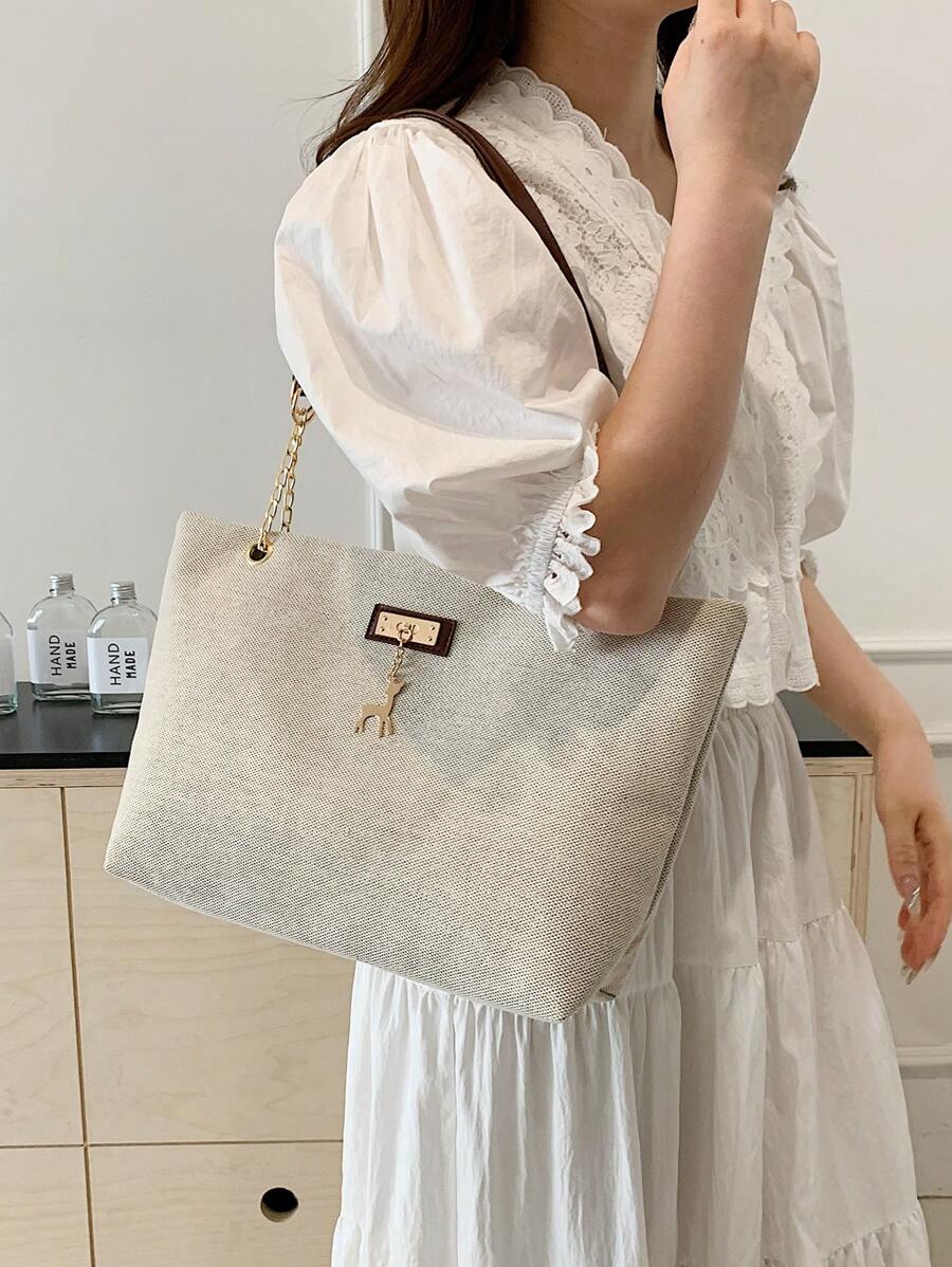 Beige large tote bag worn on shoulder showing front metal plaque gold deer charm and brown straps
