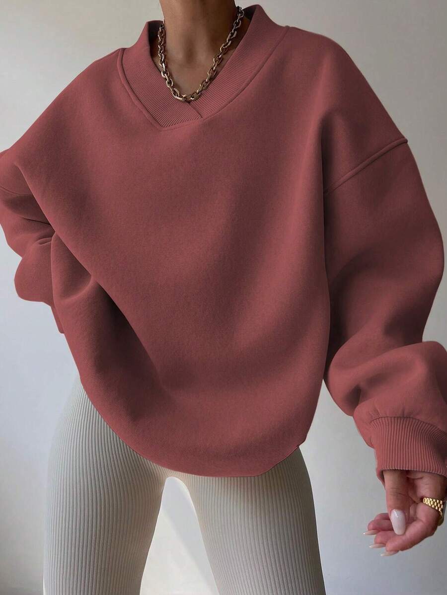 Angled front view of red oversized V-neck sweatshirt styled with beige leggings