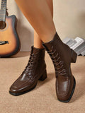 A pair of dark brown leather lace-up ankle boots with block heels, shown on a model's feet against a neutral indoor background with a guitar and books.