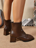 A pair of dark brown leather lace-up ankle boots with block heels, shown on a model's feet against a neutral indoor background.