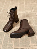 A pair of dark brown leather lace-up ankle boots with block heels, displayed on a vintage newspaper background. One boot is shown from the side, and the other is positioned to show the sole and heel.
