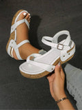 Handheld close-up of white studded wedge sandal with toe loop and patterned platform sole