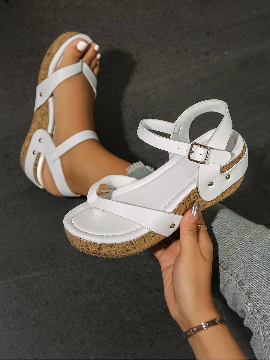 Handheld close-up of white studded wedge sandal with toe loop and patterned platform sole