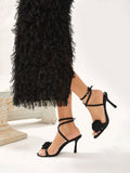 Black high-heeled sandals with floral details worn with a black ruffled dress on a white background