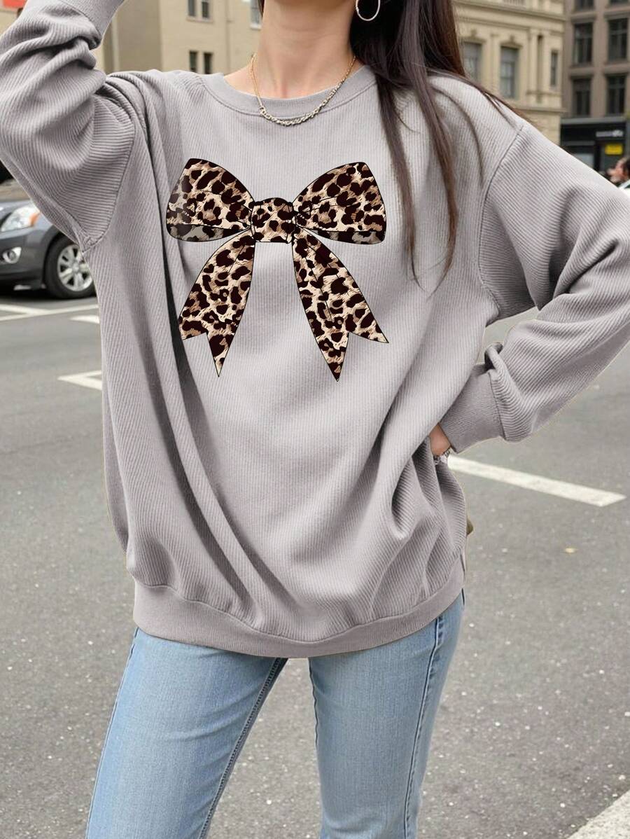 Front outdoor view of grey loose sweatshirt with large leopard bow and ribbed trim