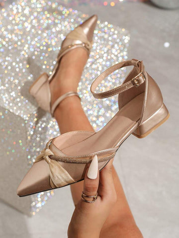 Close side view of champagne ankle-strap flat showing bow, rhinestones, buckle, and block heel
