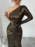 A woman wearing a one-shoulder leopard print dress with a long sleeve and ruched waist, standing against a light gray wall.