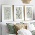 Sage green leaf and flower prints styled above a bedroom bed