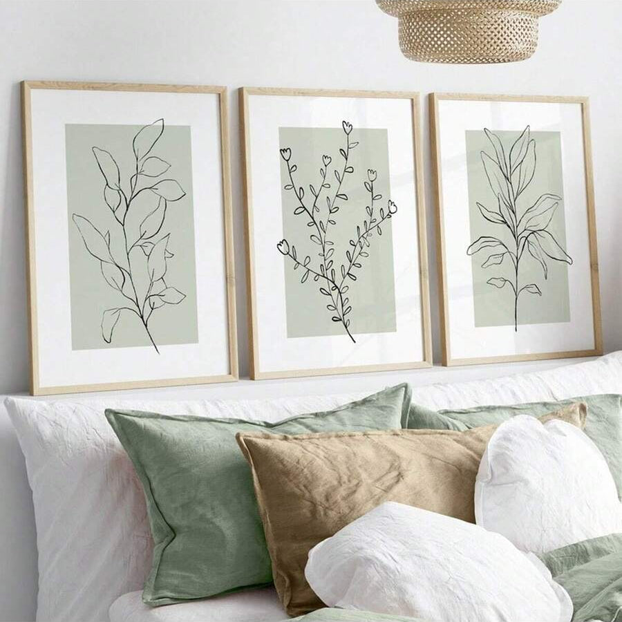 Sage green leaf and flower prints styled above a bedroom bed