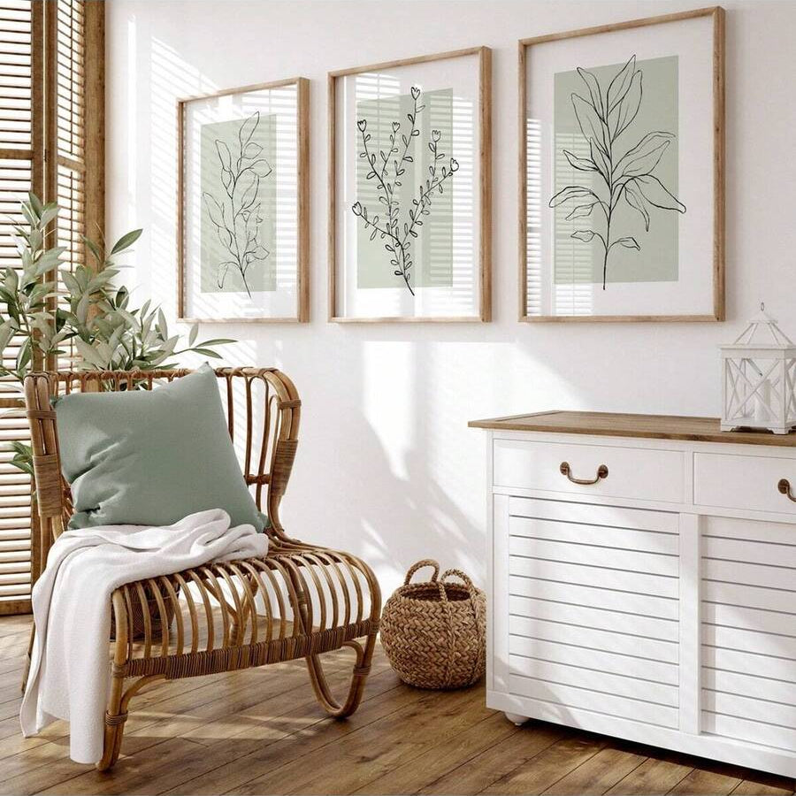 Botanical line art triptych in light wood frames over a woven chair