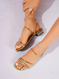 Angled view of gold open toe slide sandals with glossy straps and rhinestone band