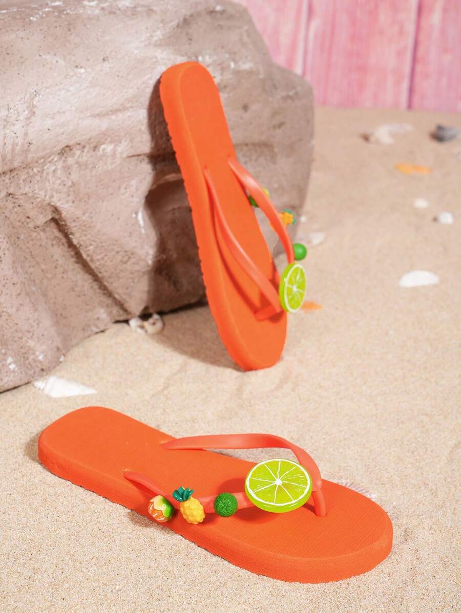 Product-only view of orange fruit charm flip-flops staged with beach shells