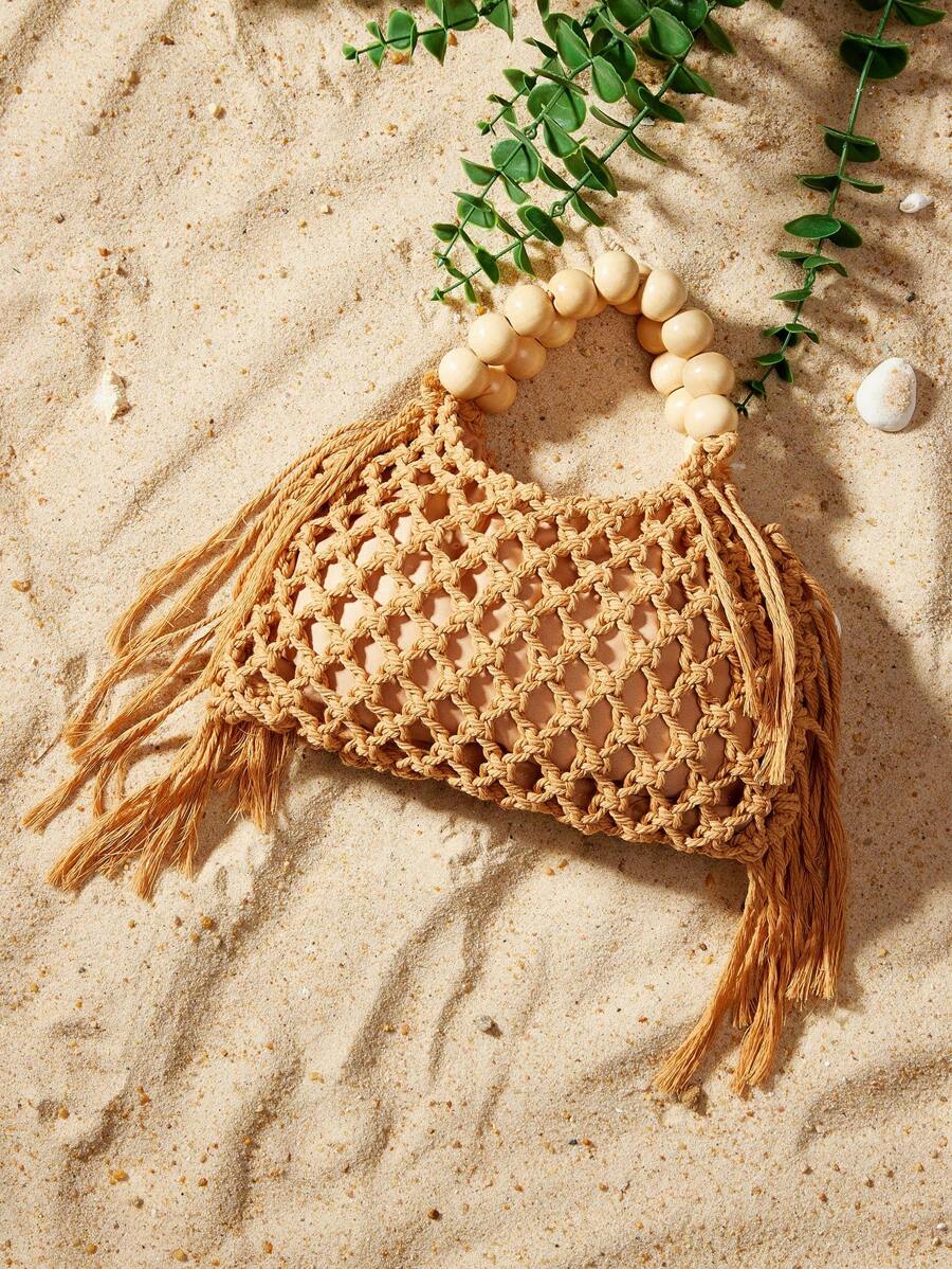 Tan crochet hollow beach bag with cream bead handle and fringe on sand