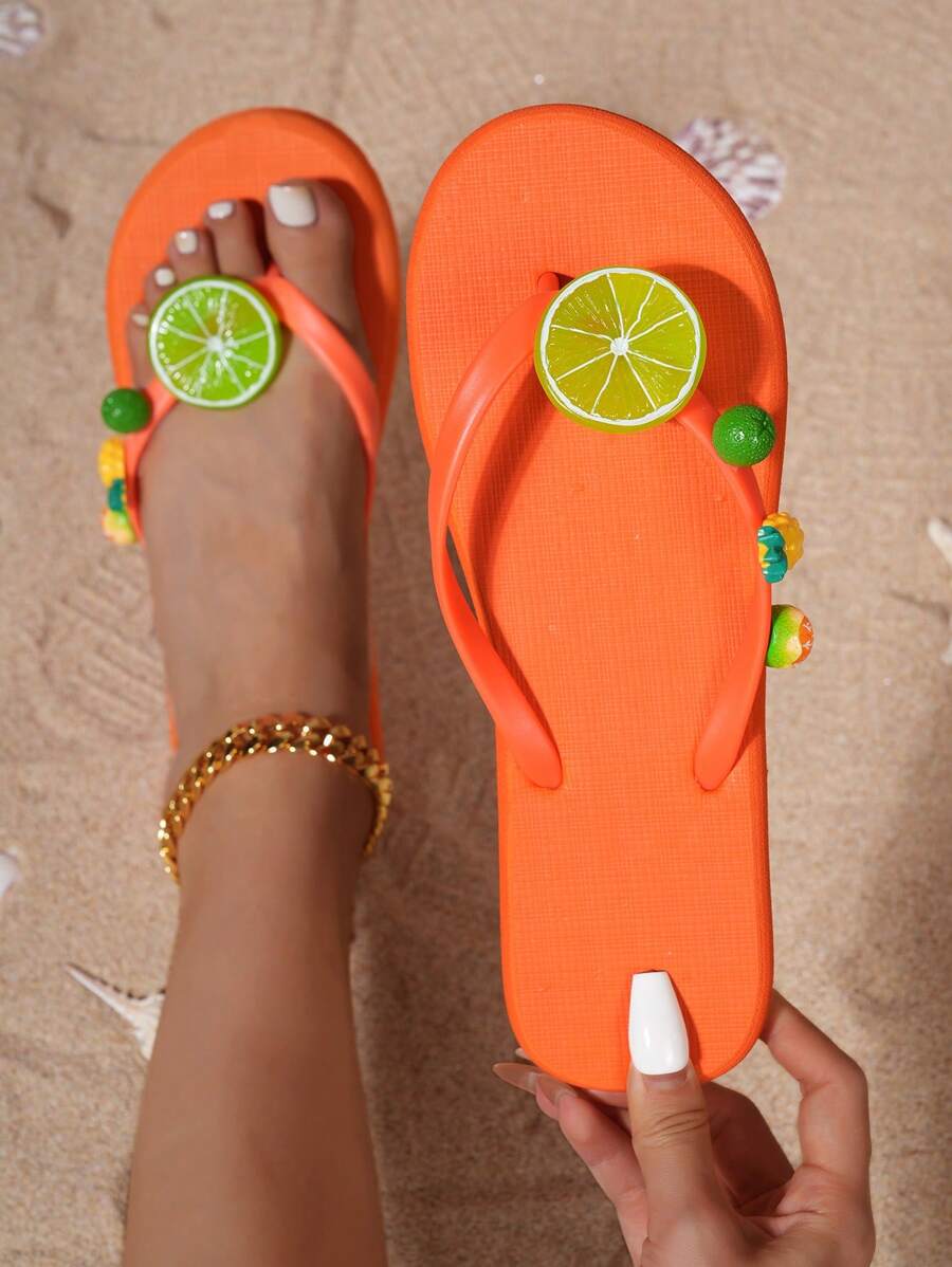 Overhead view of burnt orange fruit sandals shown worn and held on sand