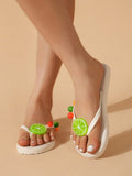Low front view of white fruit charm thong sandals on a neutral studio floor