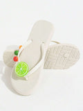 Product and outsole view of white fruit charm flip-flops on a studio surface