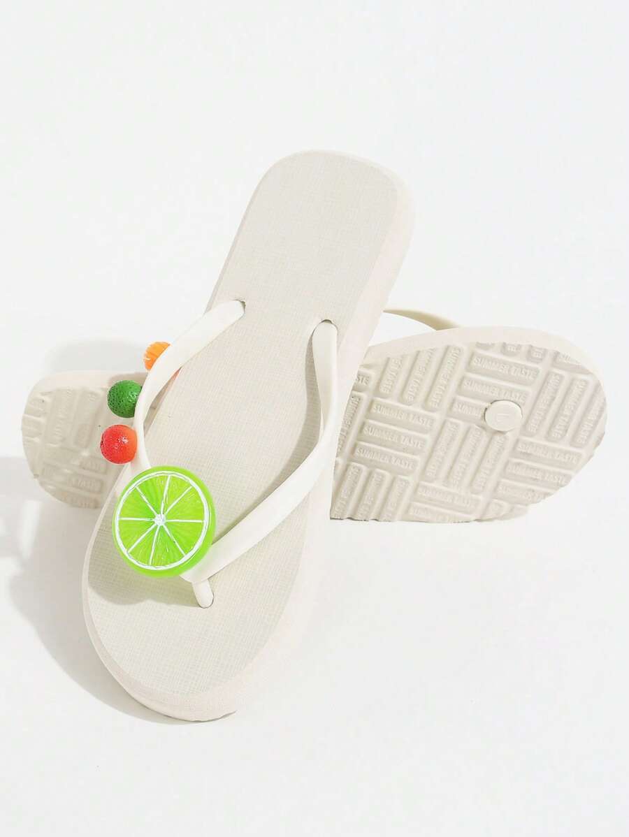 Product and outsole view of white fruit charm flip-flops on a studio surface