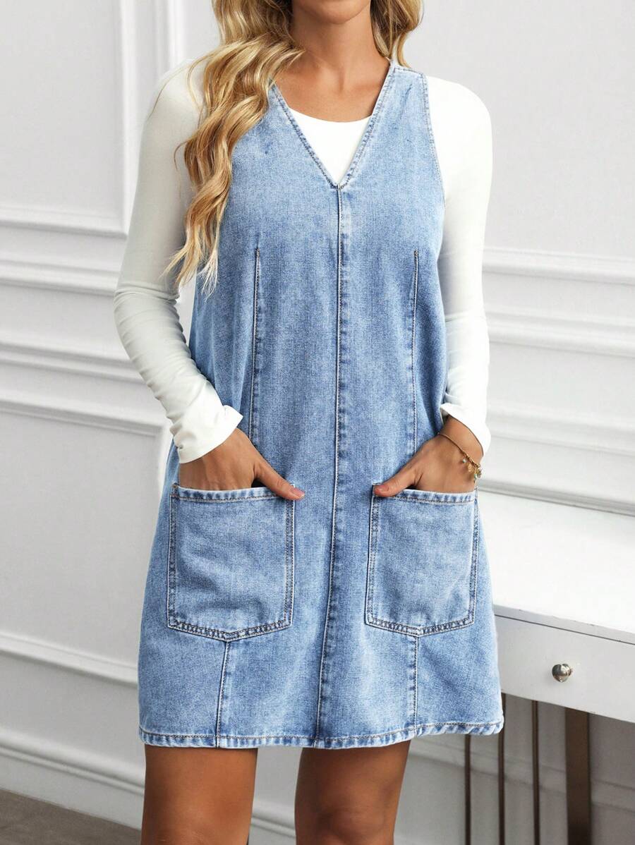 Front detail view of light-wash blue denim pinafore mini dress with center seam and pockets
