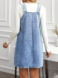 Back view of light-wash blue denim pinafore mini dress layered over a white long-sleeve top