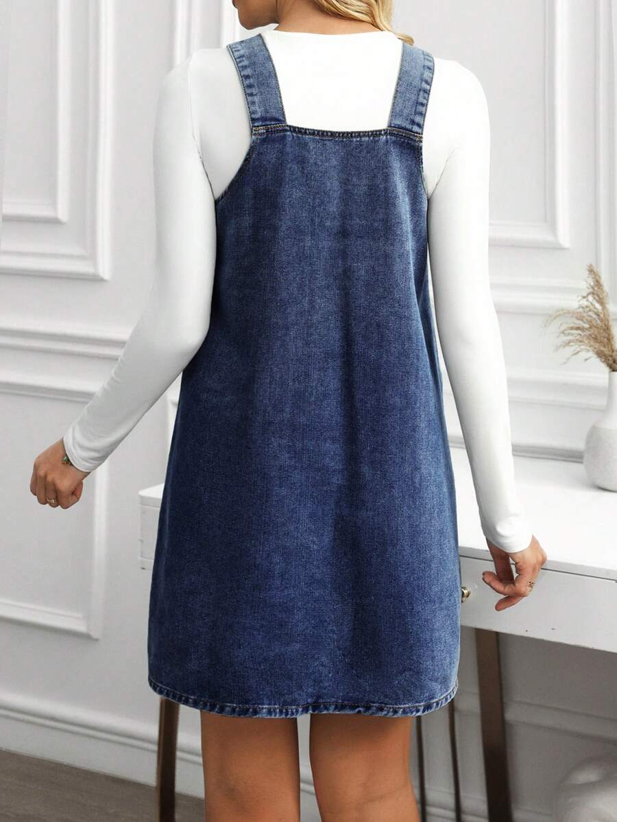 Back view of deep blue denim pinafore dress showing square back and softly faded texture