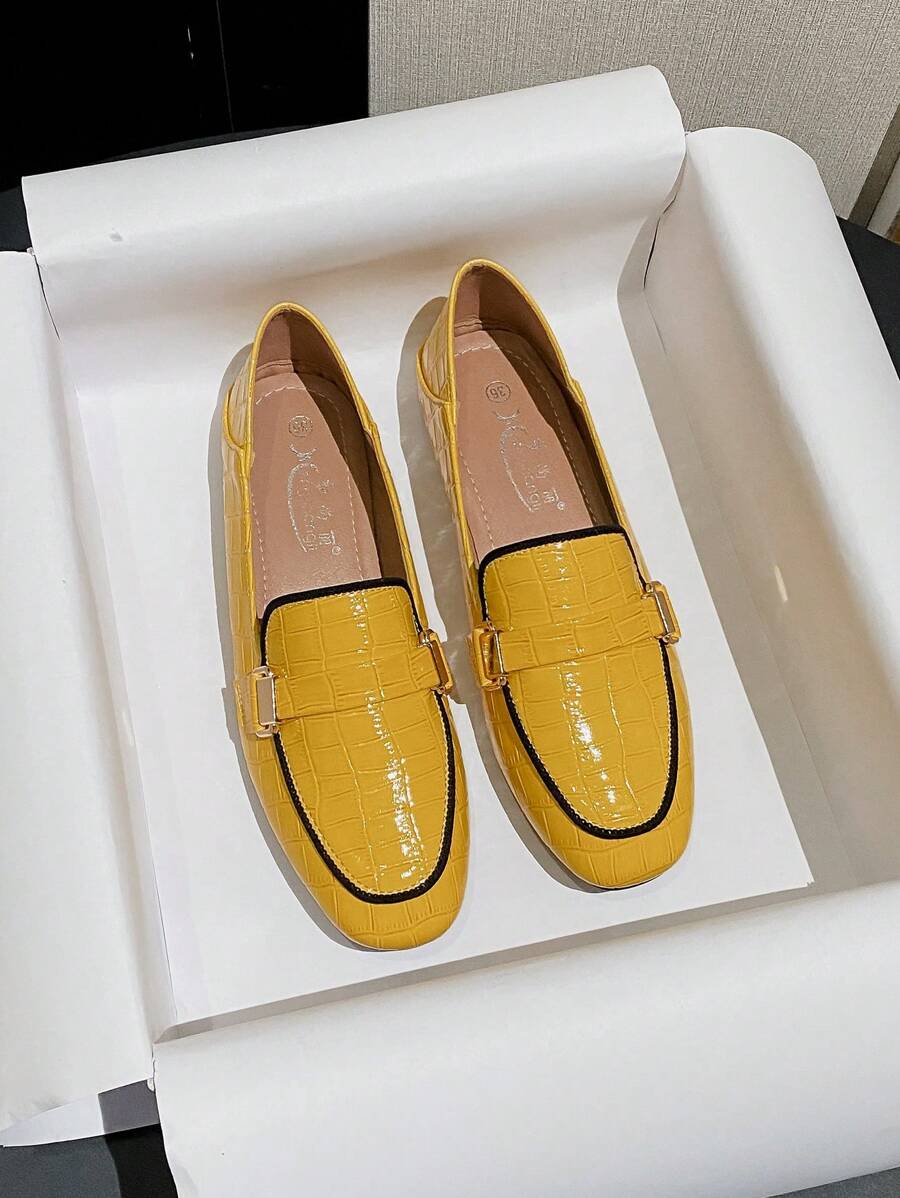 Side view of yellow slip-on loafer with black trim and gold buckle bit