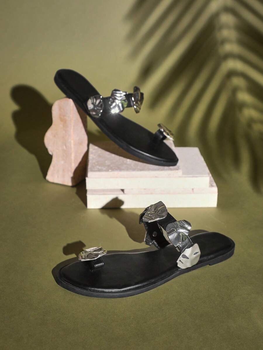 Side view of black toe-ring flat sandals with sculptural silver metal accents