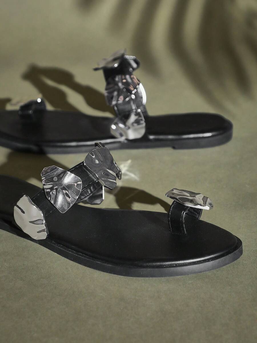 Close-up of black toe-ring flat sandal straps and sculptural silver metal details