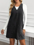 Full front view of washed black denim pinafore mini dress with deep V neck and patch pockets