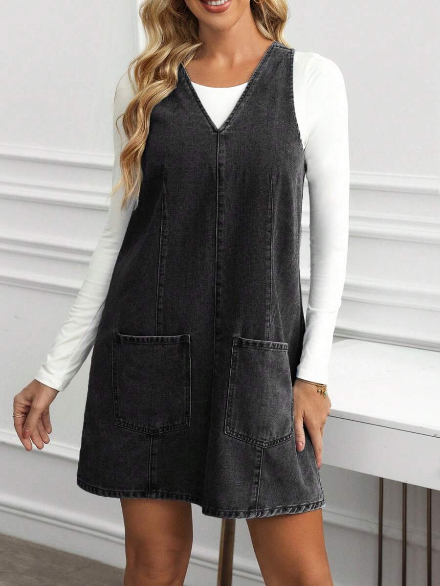 Full front view of washed black denim pinafore mini dress with deep V neck and patch pockets