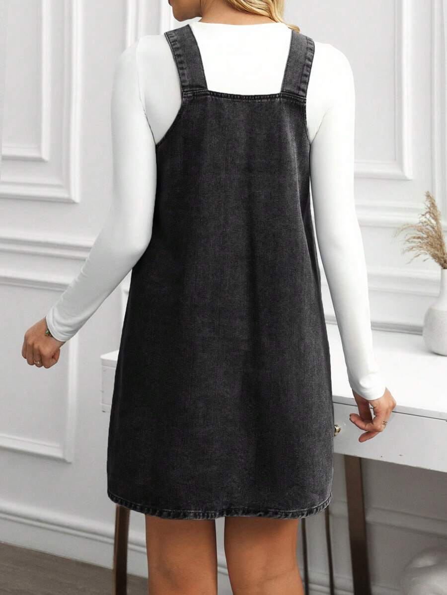 Back view of washed black denim pinafore dress showing square back and clean stitched hem