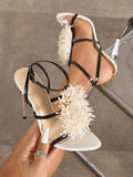 Handheld front view of black and white 3D floral cross-strap square-toe stiletto sandals with metallic heel