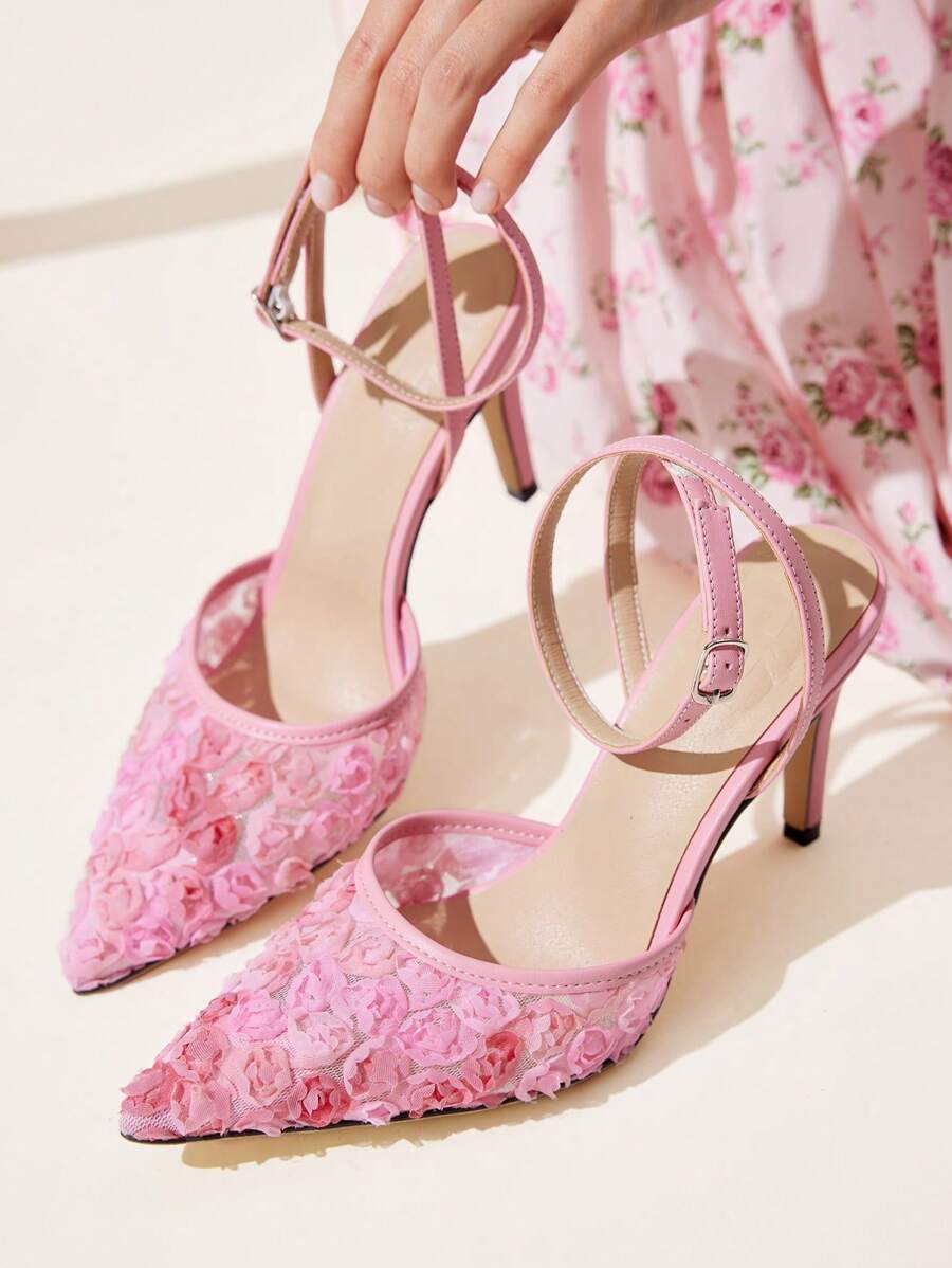 Pink floral pointed-toe ankle strap pumps with slim high heels held beside pink floral dress